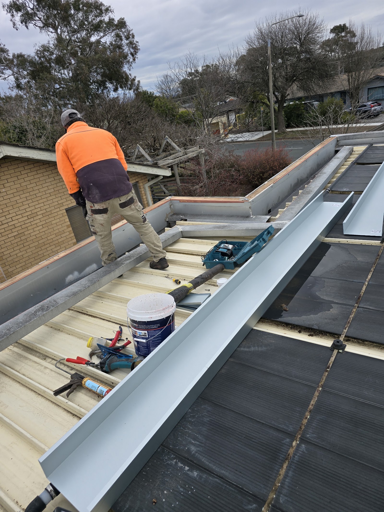 Roofer fitting new box gutter and flashing on a metal roof