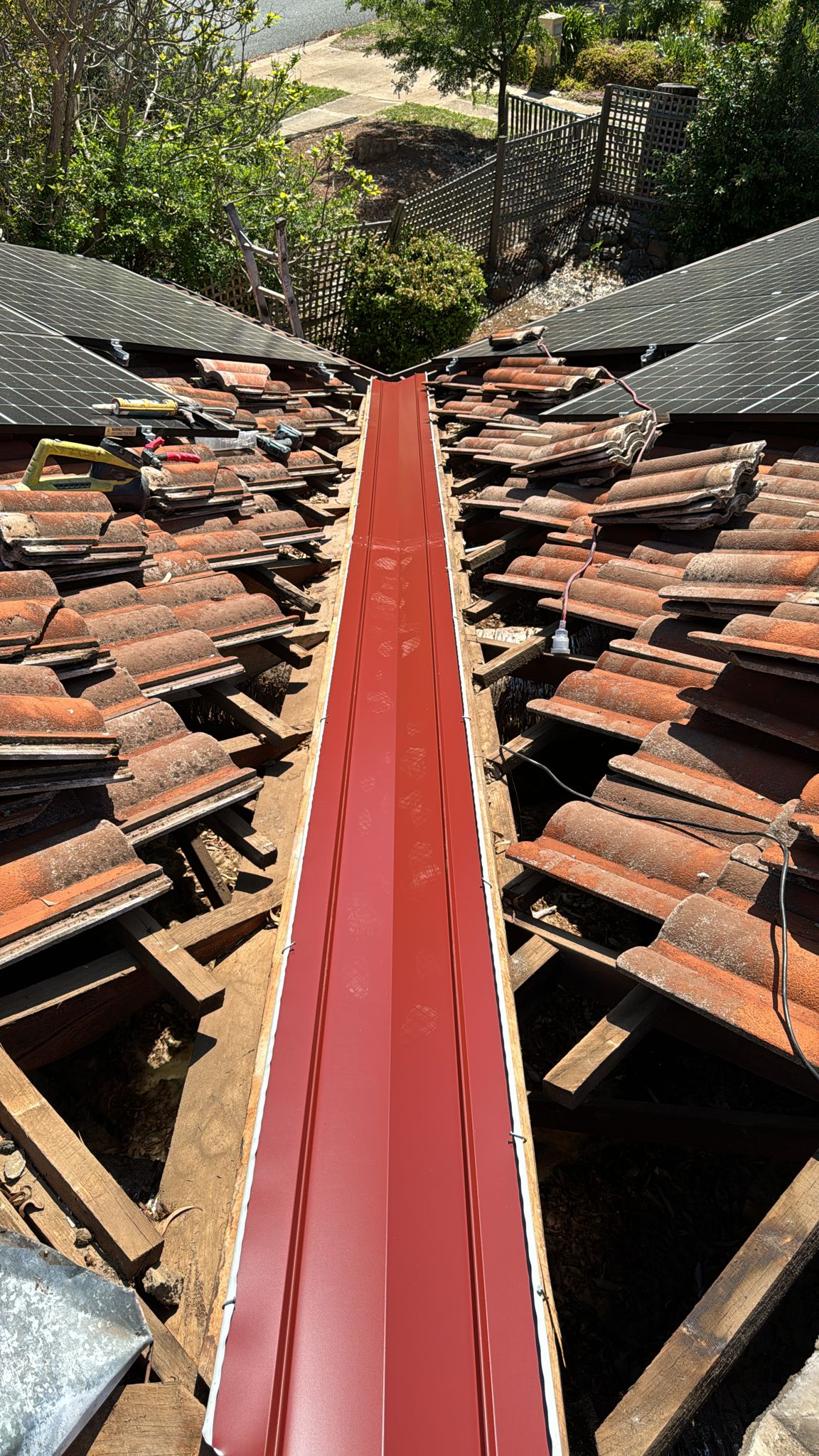 New valley iron installed between two roof sections with tiles lifted either side