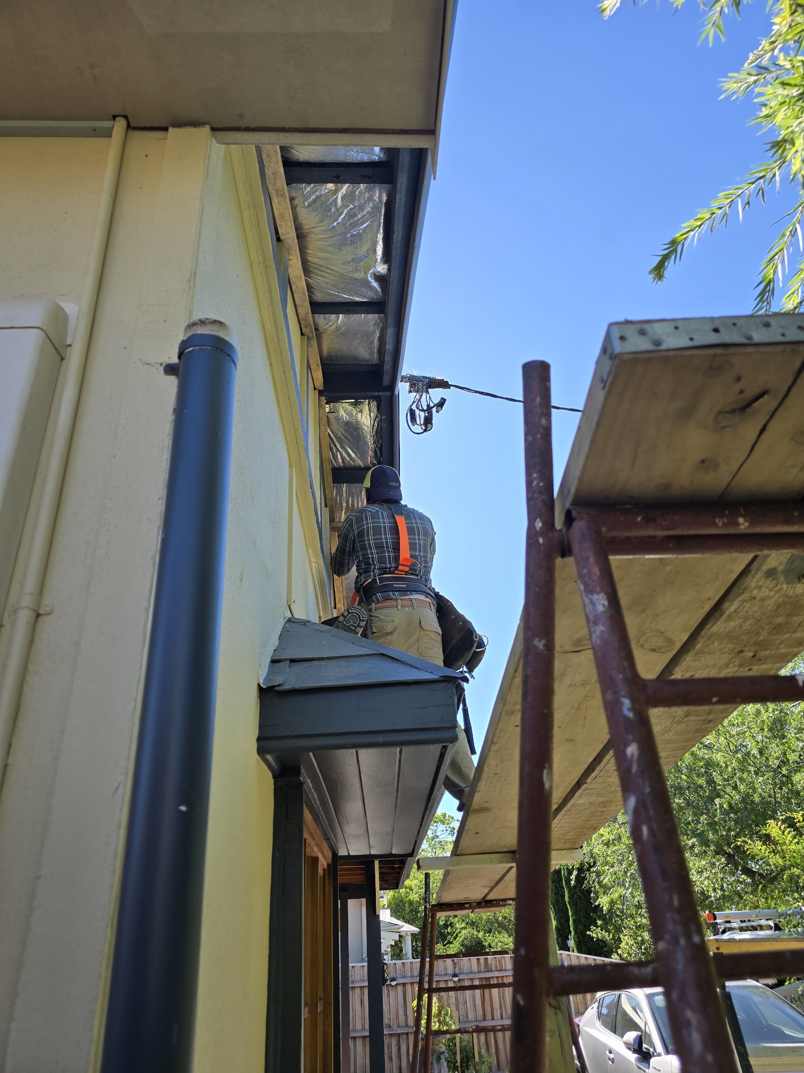Roofer in a harness working on the eaves and fascia, scaffolding alongside